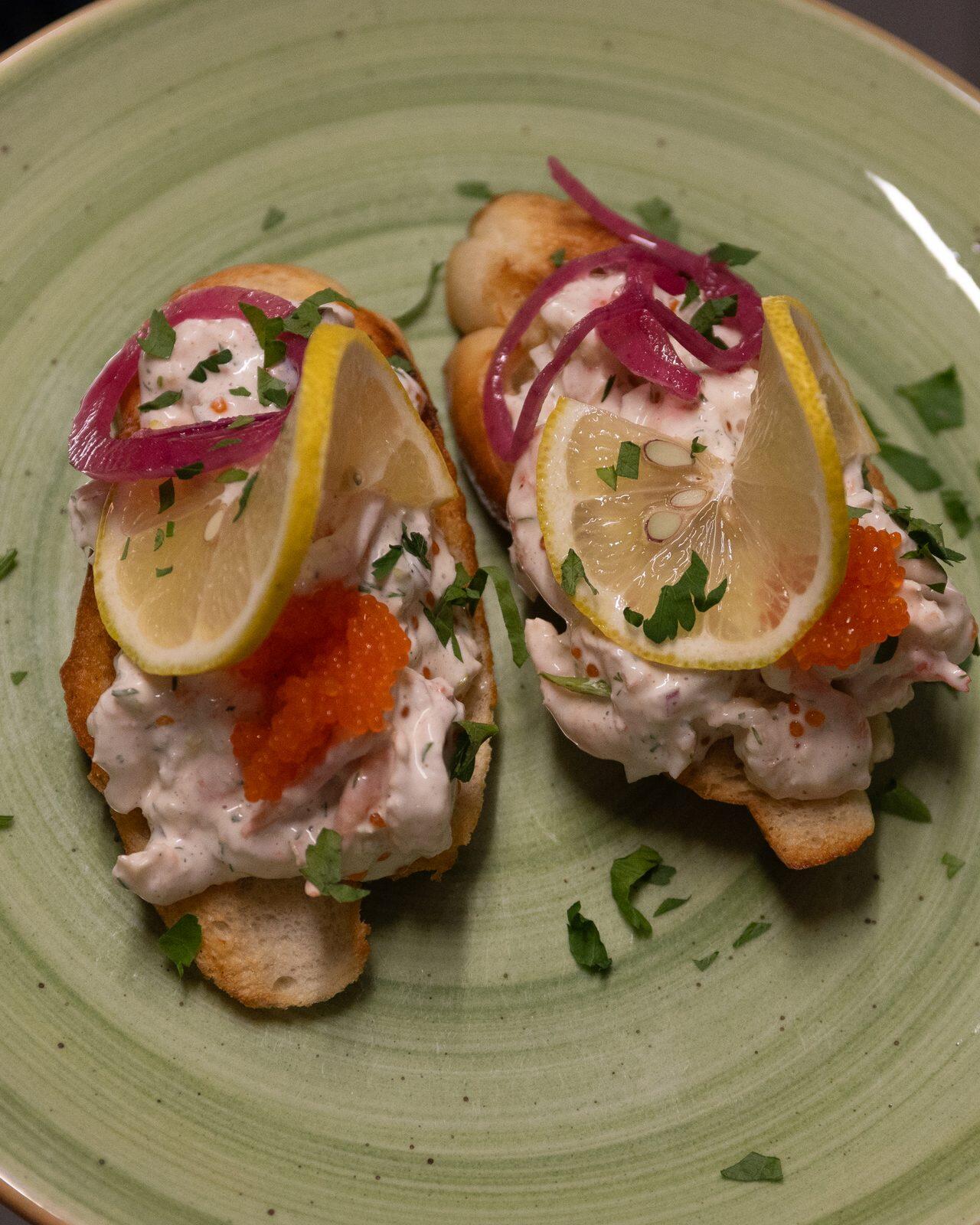 Två toast med krämig röra, rom, rödlök och citron på en grön tallrik.
