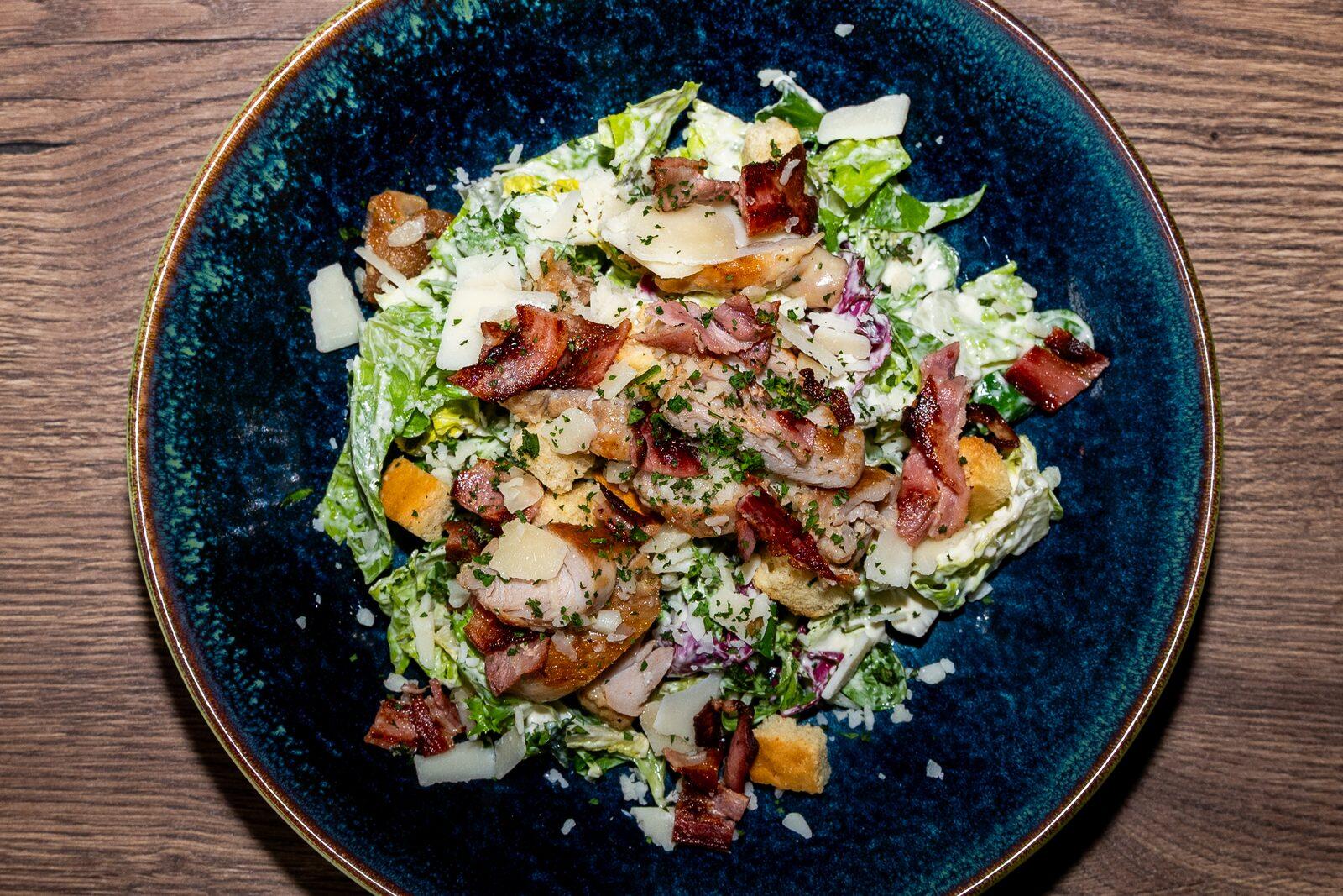 Caesarsallad med kyckling, bacon, krutonger och ost på en blå tallrik.