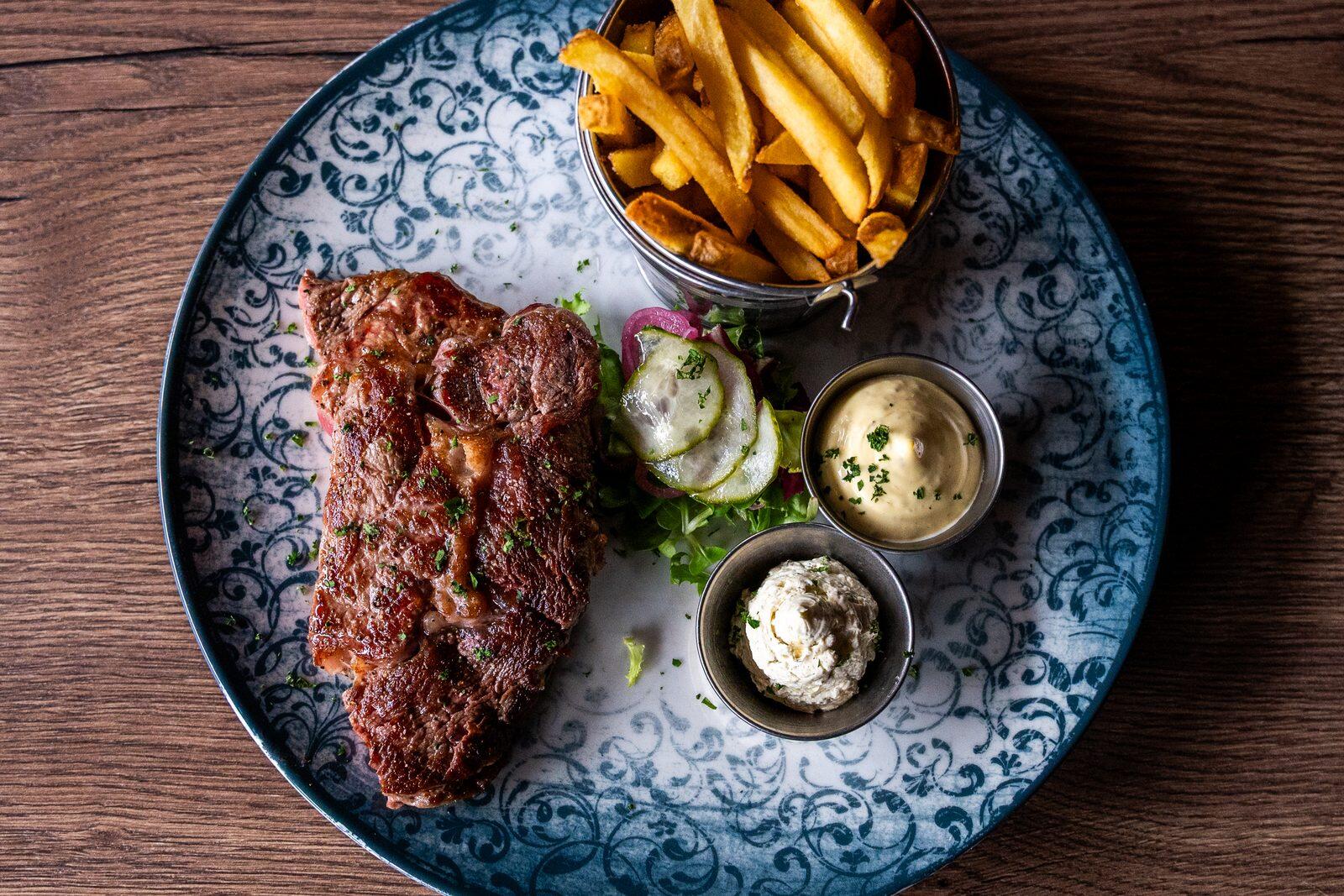 Entrecôte med pommes frites, sallad och två såsskålar på en mönstrad tallrik.