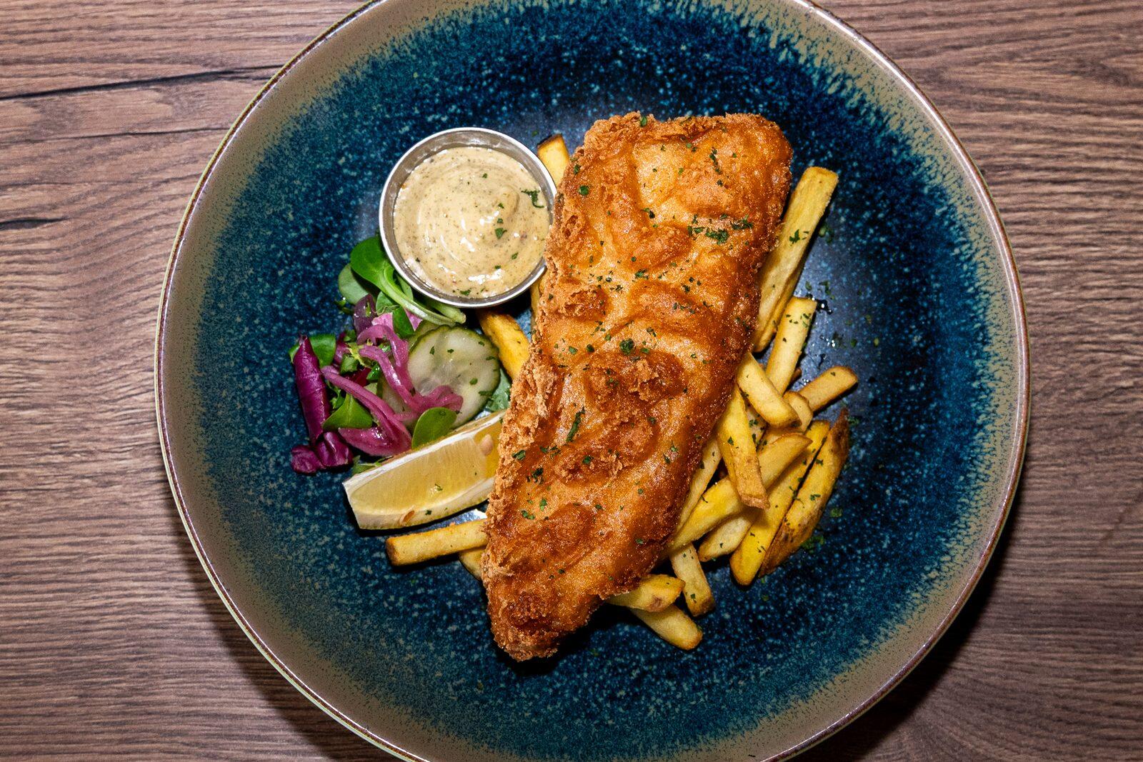 Friterad fisk med pommes frites, citron och sås på en blå tallrik.